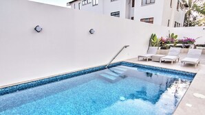 A swimming pool with clear blue water, surrounded by a white wall and a few lounge chairs. - Oceanview Penthouse Condo in Sunny Bucerias (Bucerias)