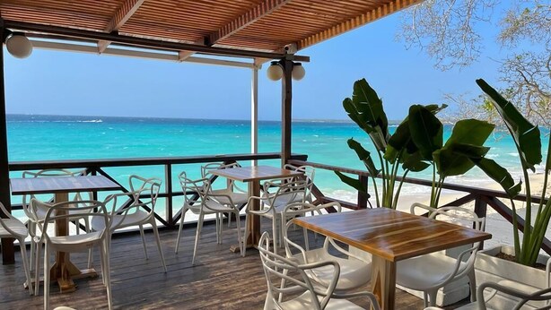 An outdoor seating area with white chairs and tables, overlooking a turquoise sea. - HOTEL PLAYA SURF BARÚ (Cartagena)