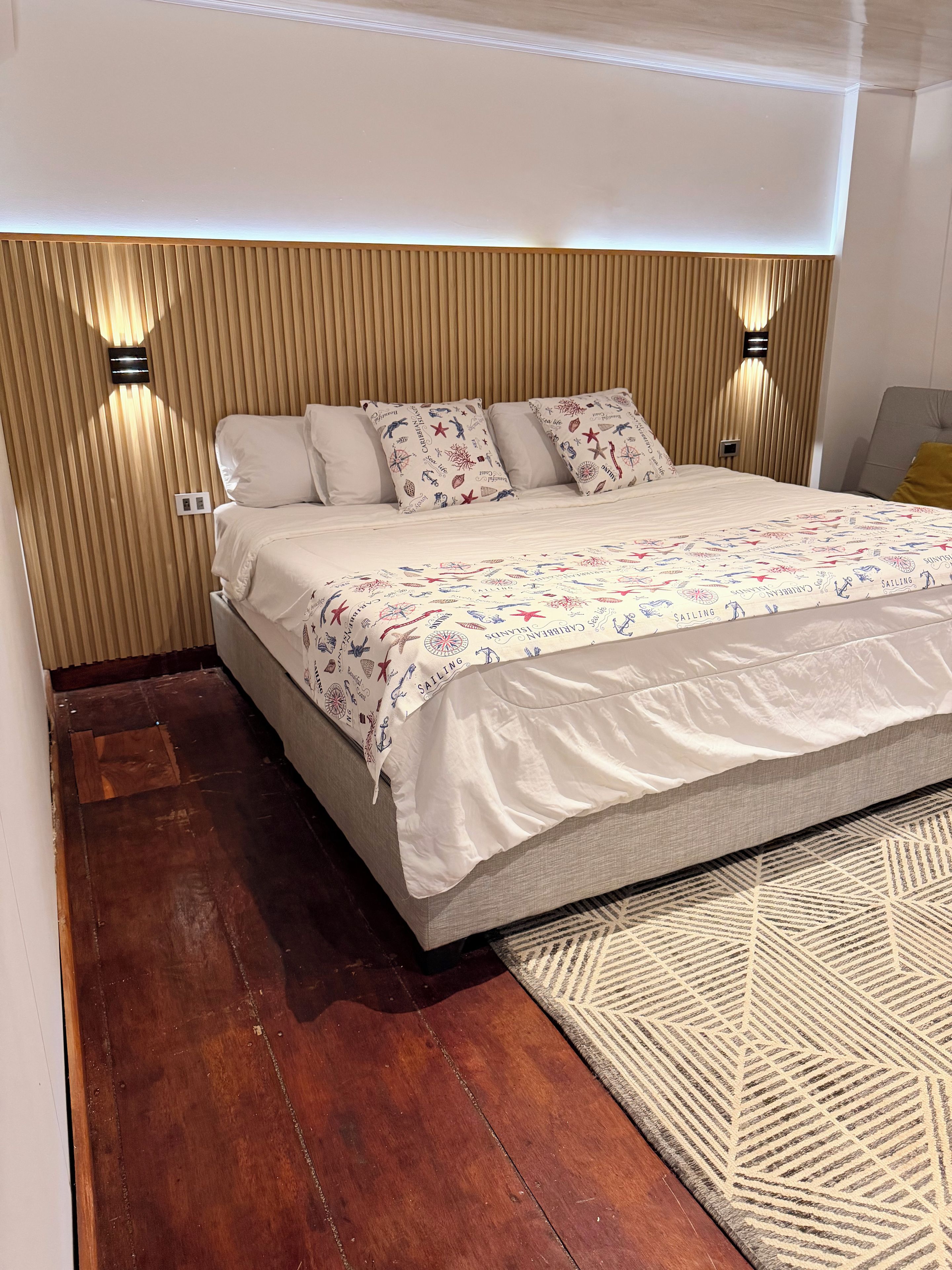 Ein Schlafzimmer mit einem Bett, einem Kopfteil, Nachttischlampen und einem gemusterten Teppich.