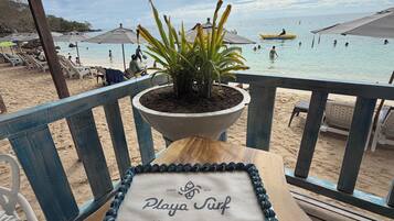 Ein Tisch direkt am Strand mit einer Torte mit der Aufschrift 'Playa Surf' und einem Topfpflanzen.