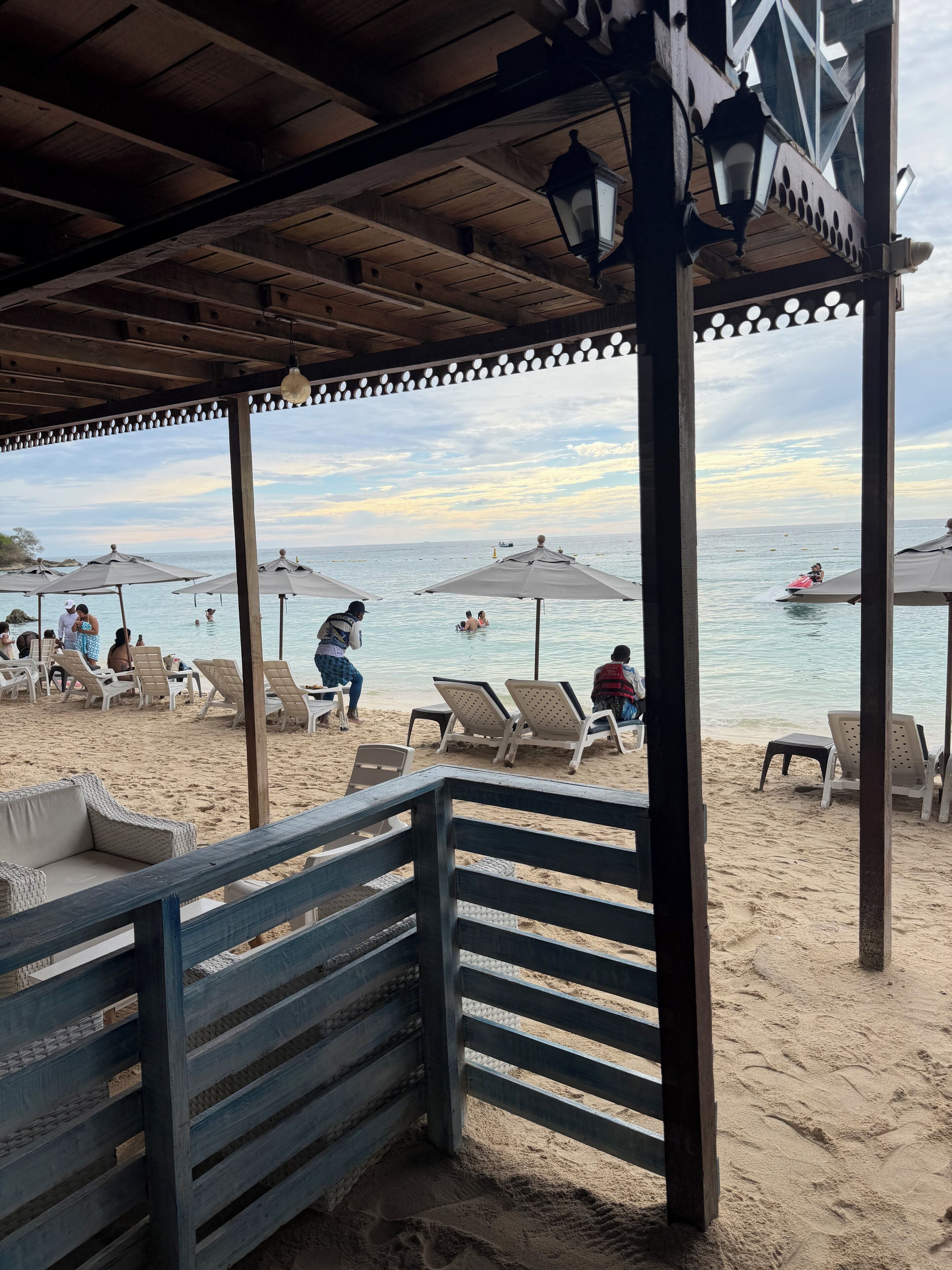A beachside area with lounge chairs, umbrellas, and a wooden pergola overlooking the sea.