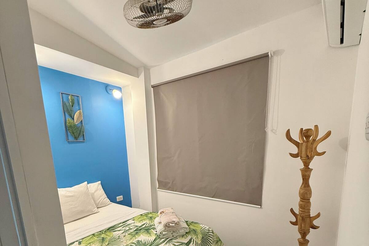 Quarto com cama, ventoinha no teto, janela com persiana e objeto decorativo de madeira.