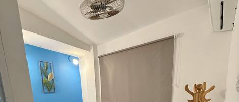 A bedroom with a bed, a ceiling fan, a window with a blind, and a wooden decorative piece.