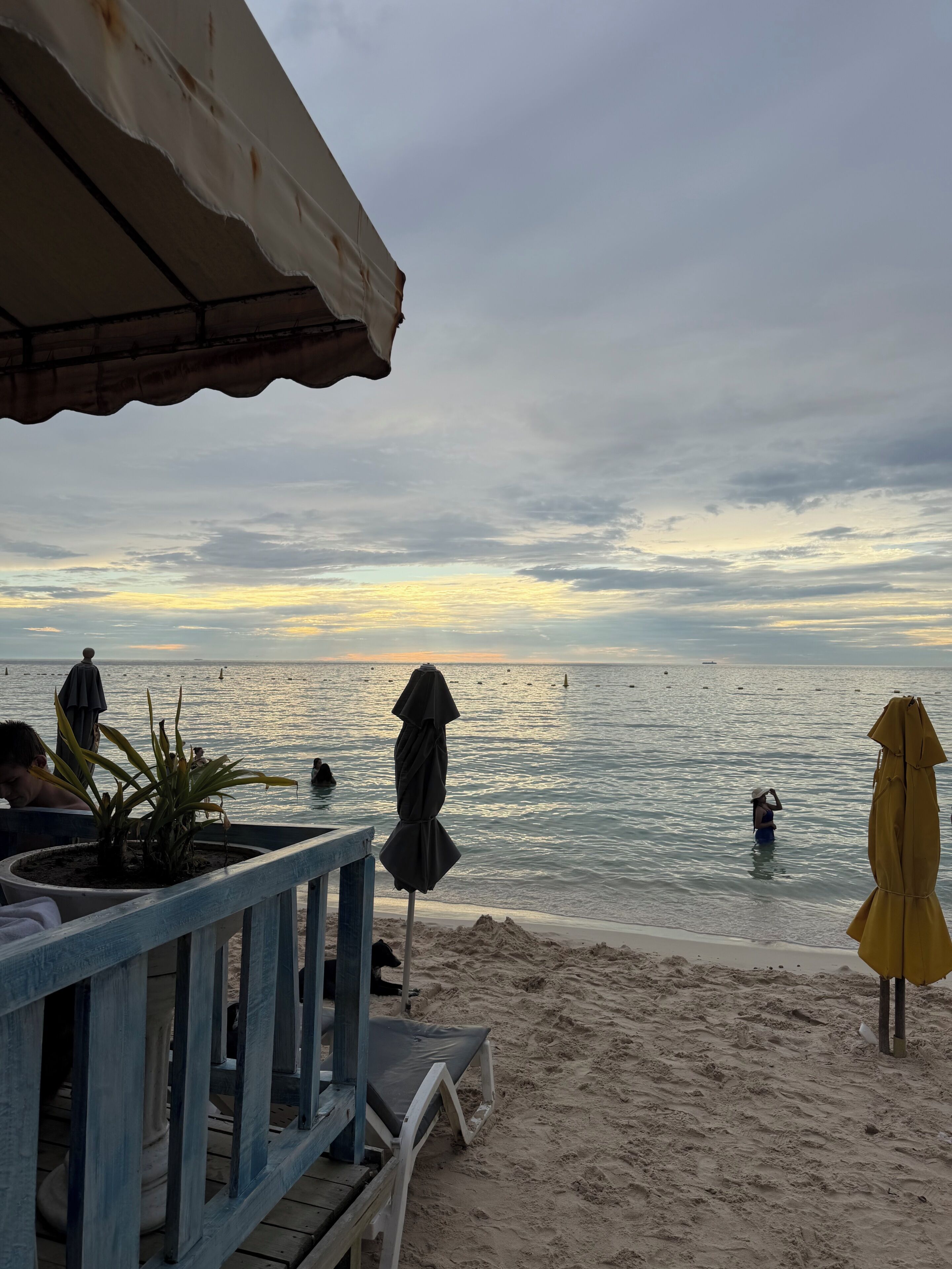 A beachside view with a wooden deck, umbrellas, and a sandy beach.