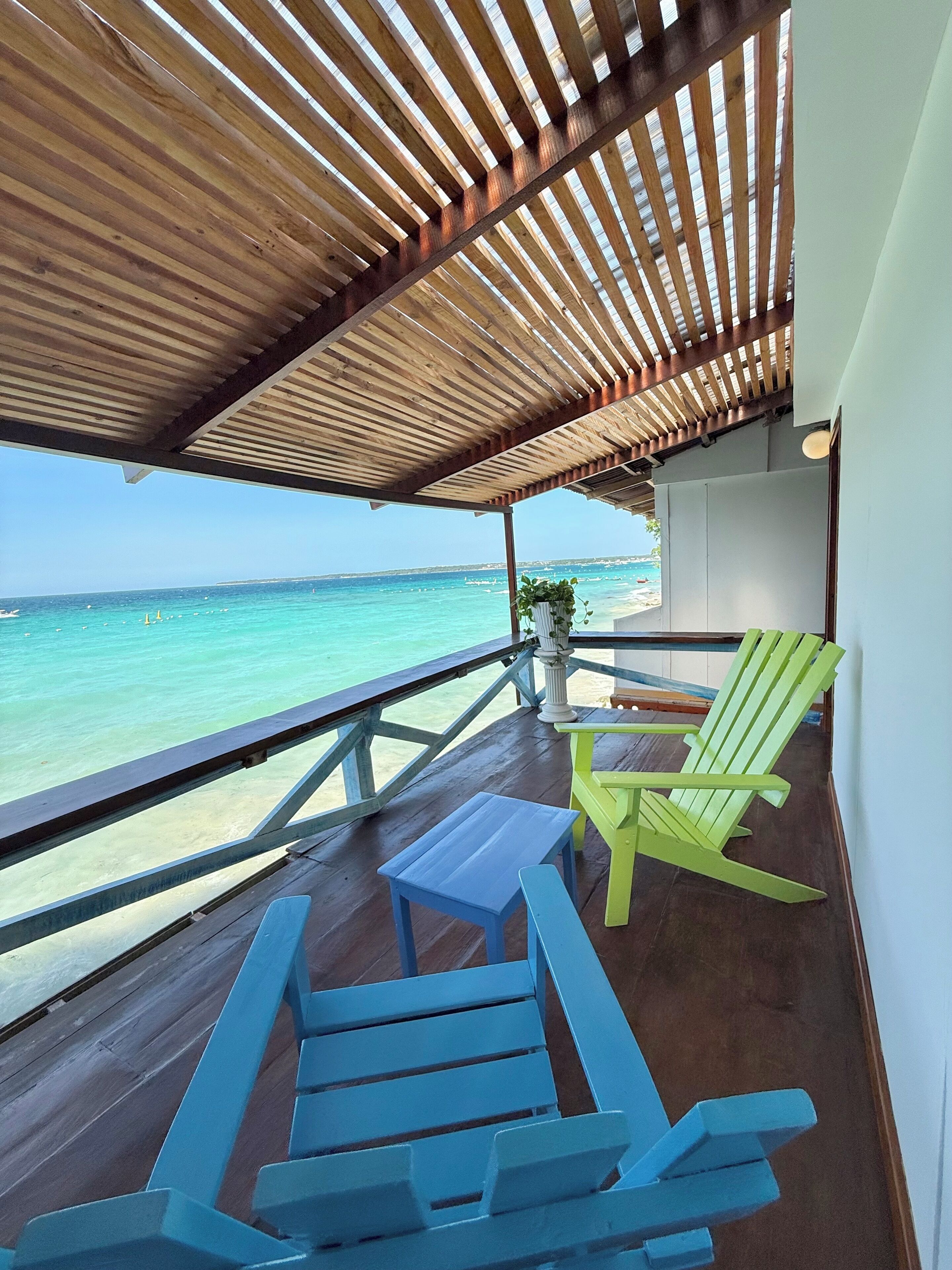 A wooden deck with a view of the ocean, a railing, and two colorful chairs.
