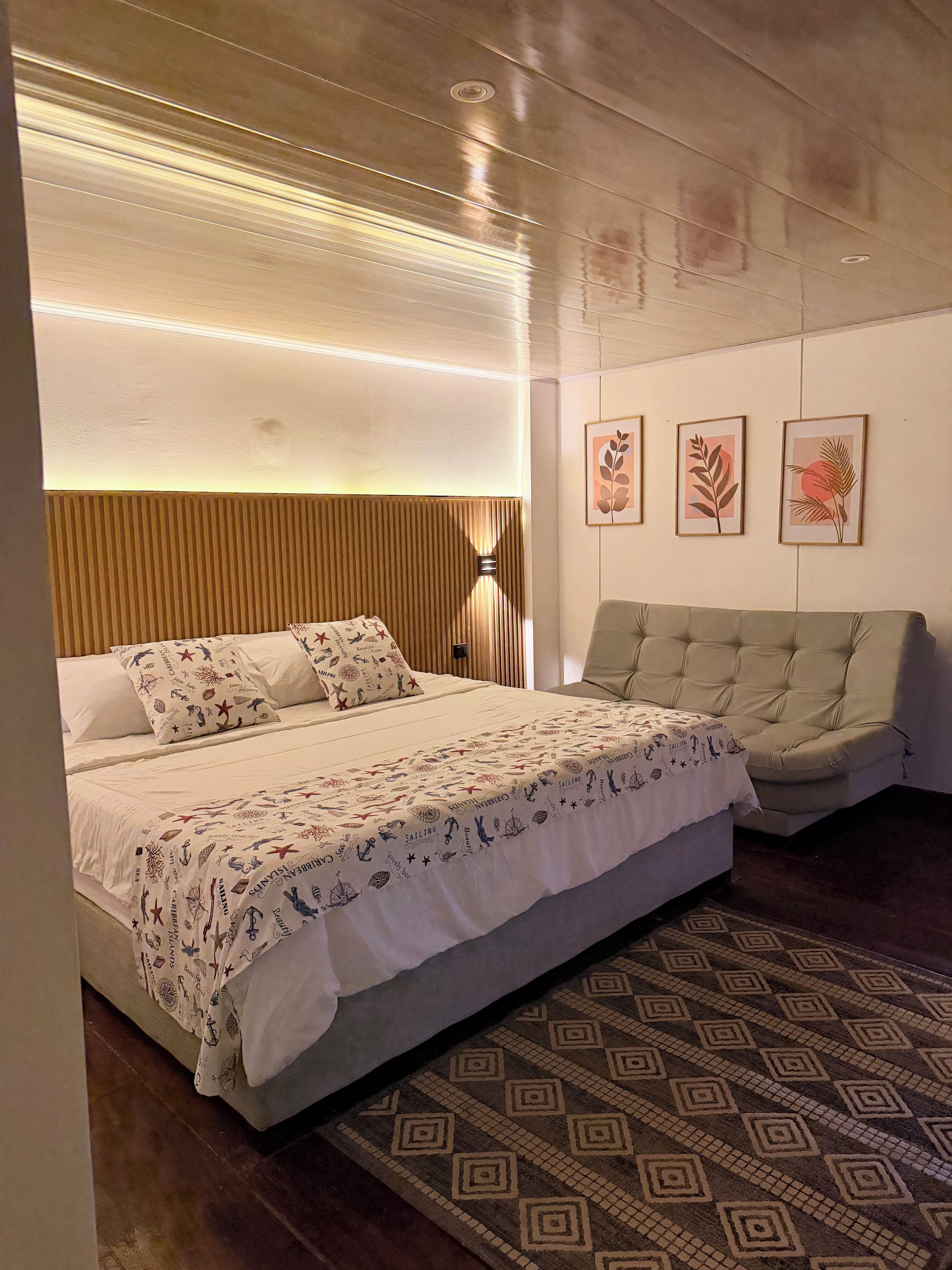 Quarto moderno com cama, sofá, tapete estampado e obras de arte na parede.