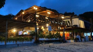 A beachside building with a covered outdoor area, multiple light fixtures, and potted plants. - HOTEL PLAYA SURF BARÚ (Cartagena)