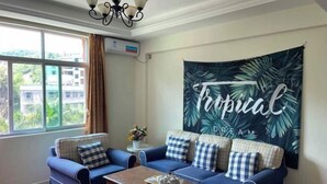 A room with a blue sofa set, a wooden coffee table, and a tropical-themed tapestry on the wall. - FenYangJu Hotel (Longmen)