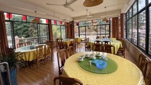 A spacious dining area with round tables and chairs, large windows with red decorations, and ceiling fans. - FenYangJu Hotel (Longmen)