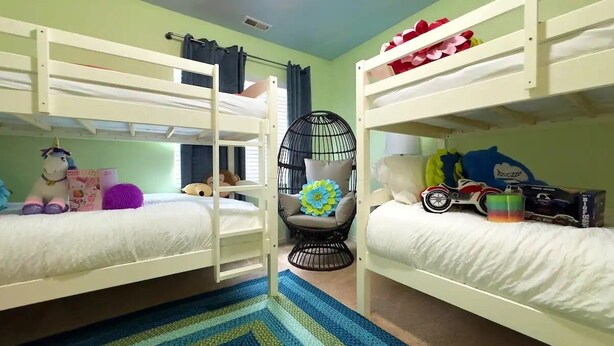 Une chambre avec des lits superposés, un tapis rayé bleu et vert, une chaise noire avec un coussin à motifs floraux et des jouets sur les lits.