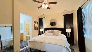 A hotel room with a bed, a ceiling fan, a TV mounted on the wall, and a window with curtains.