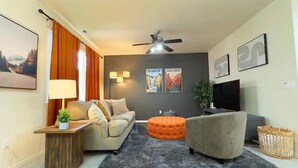 A modern living room with a sofa, ottoman, and a TV.