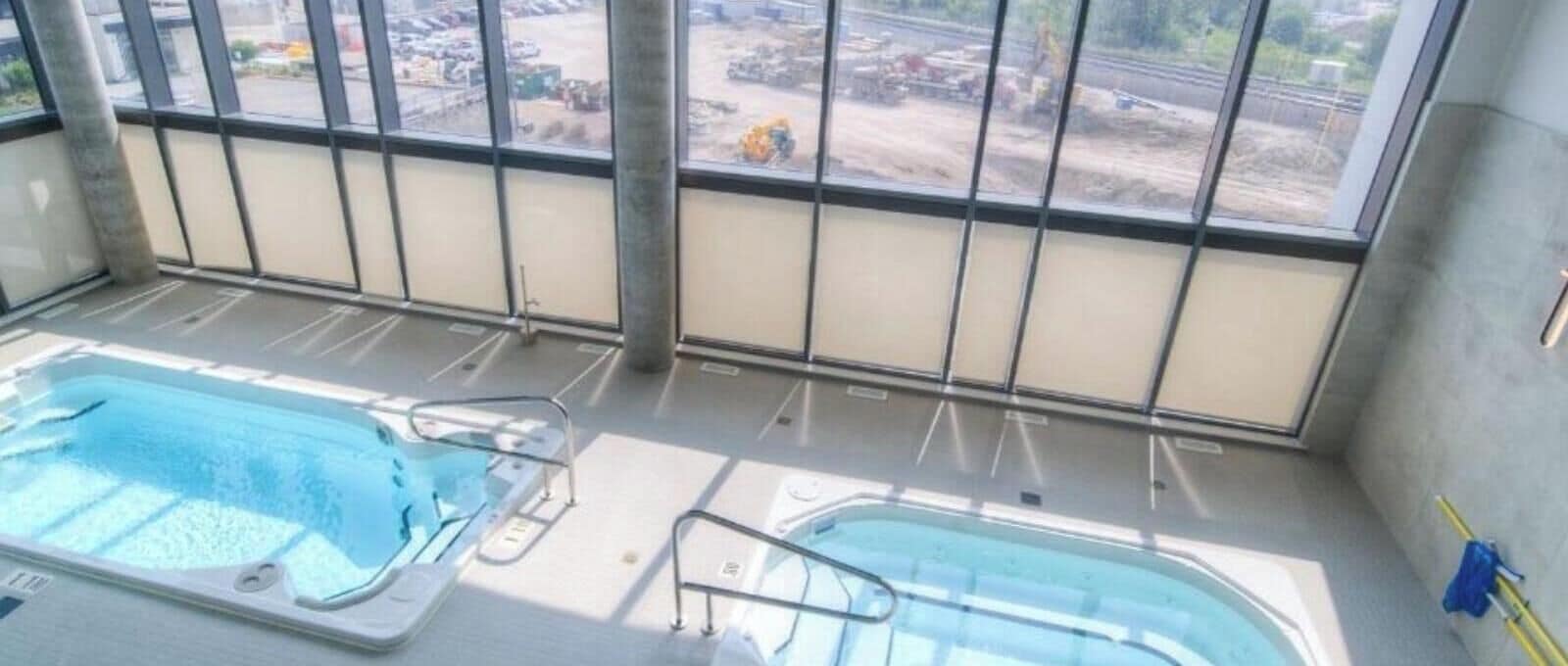 A pool area with two hot tubs and a view of a construction site through large windows.