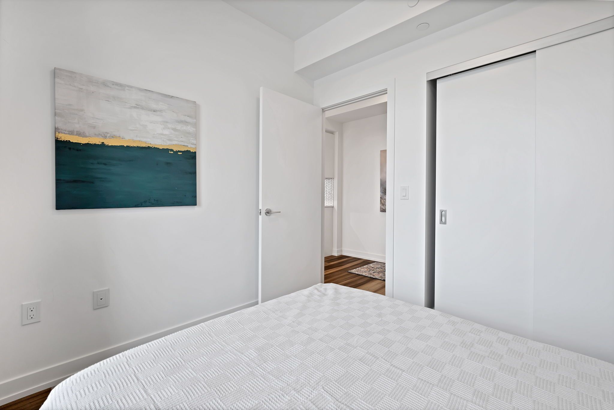 A bedroom with a bed, a painting, and white doors.