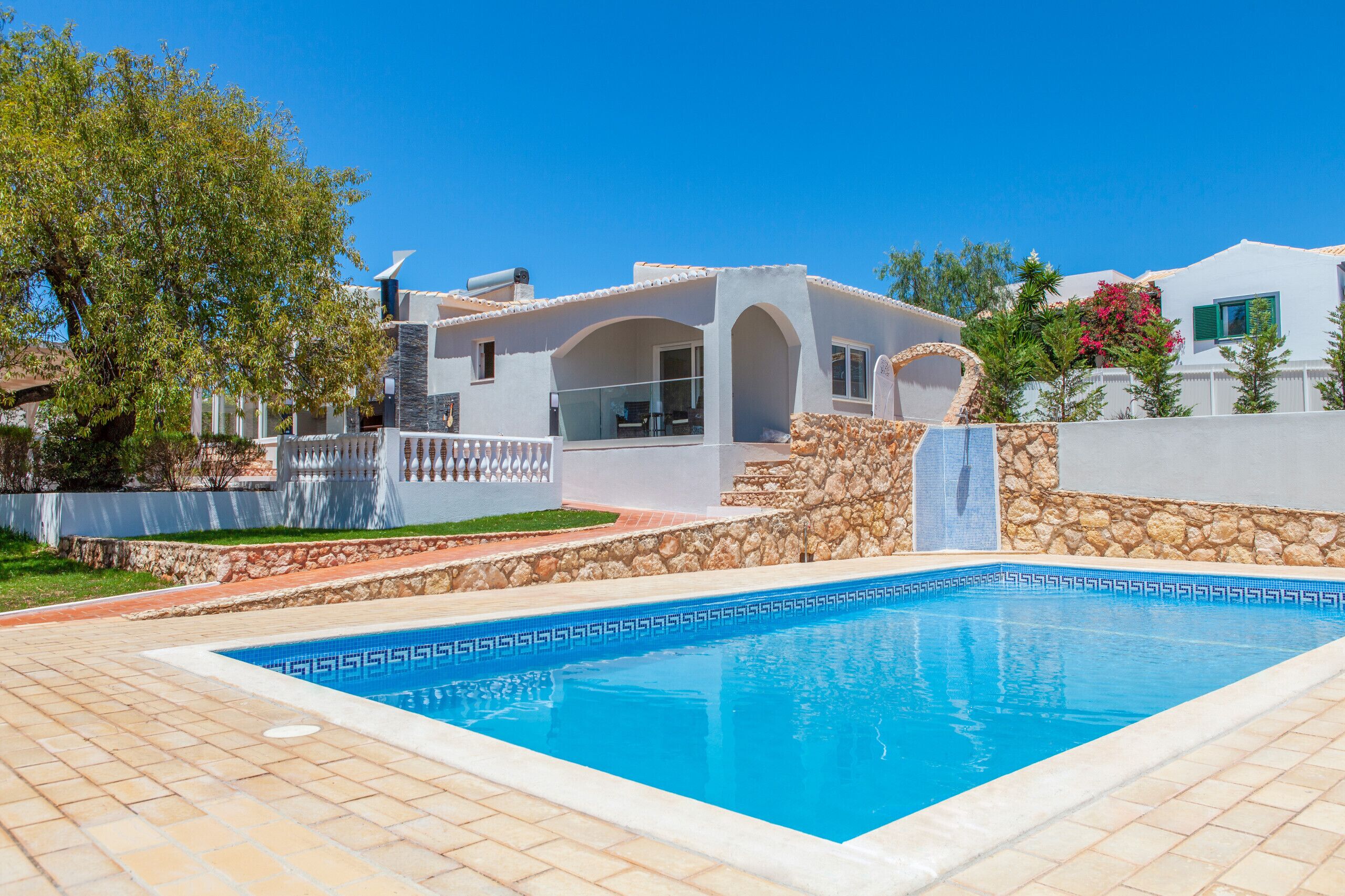 A modern villa with a swimming pool, stone walls, and a clear blue sky.
