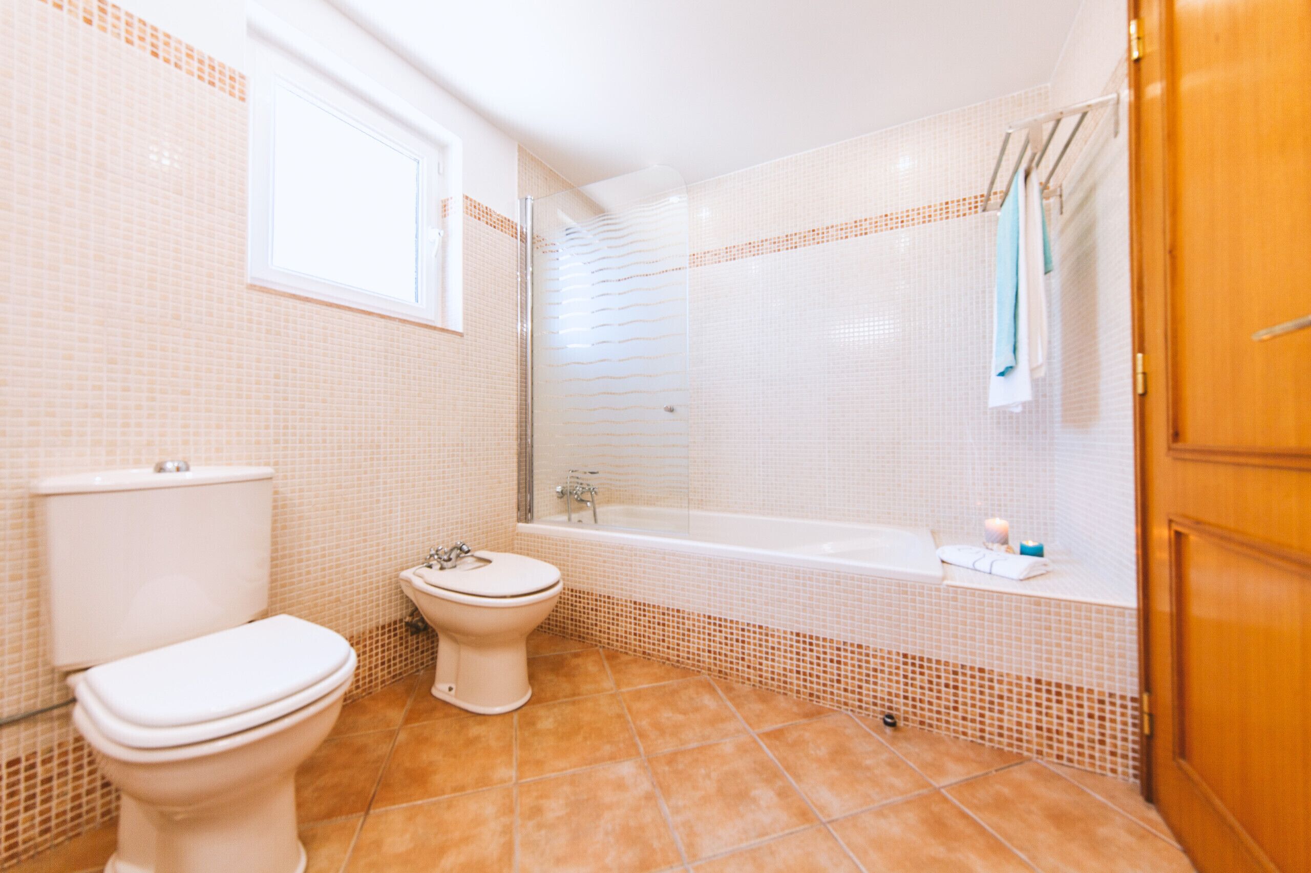 A bathroom with a toilet, bidet, and bathtub, tiled in a light color scheme.