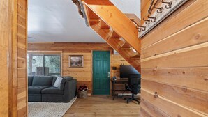 Um interior em madeira com uma porta verde, um sofá cinza e uma escrivaninha.