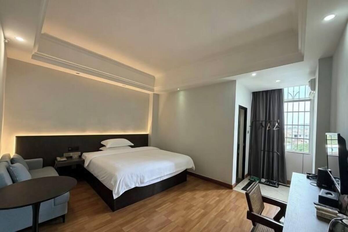 A modern hotel room with a bed, bedside table, desk, and chair.