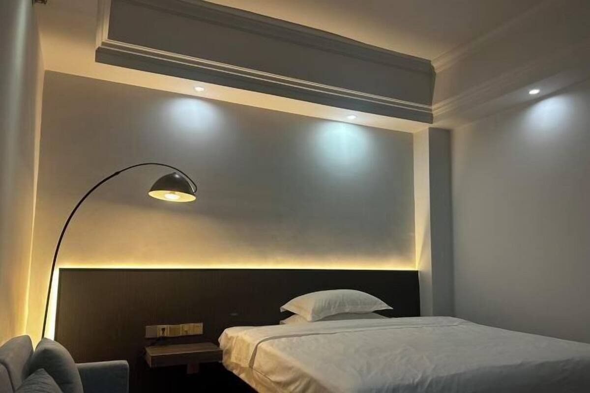 A hotel room with a bed, a bedside table, a lamp, and a headboard.