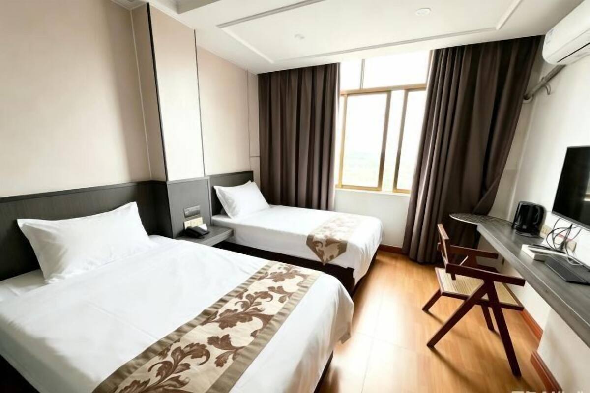 A hotel room with two beds, a desk, a chair, and a television.