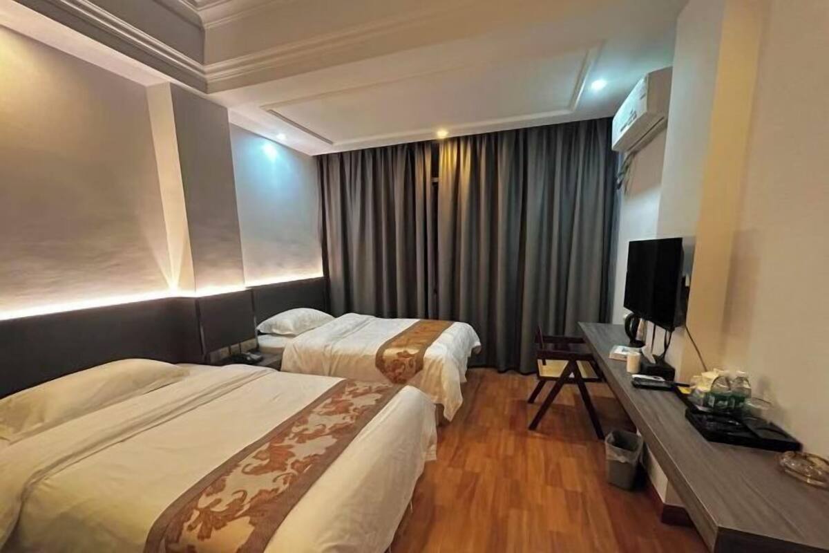 A hotel room with two beds, a desk with a chair, a TV, and a window with curtains.