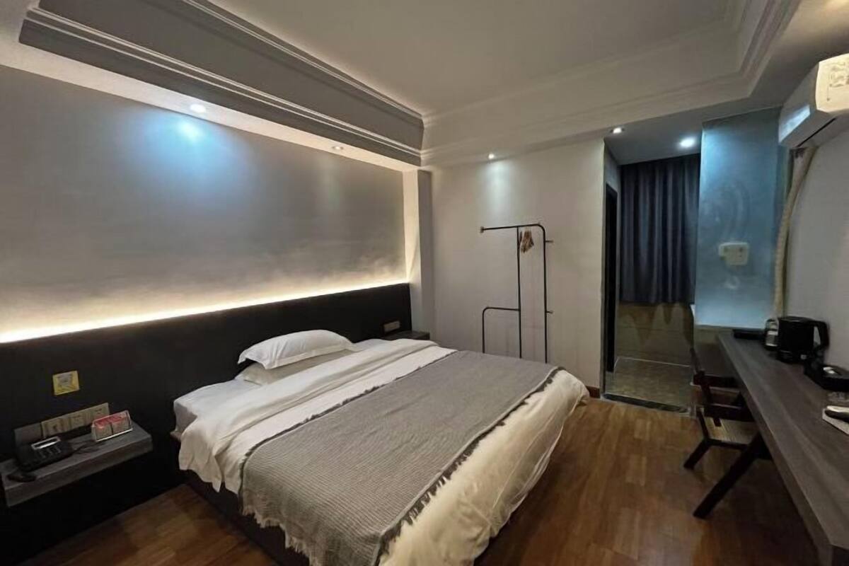 A hotel room with a bed, bedside table, desk, and a mirror.