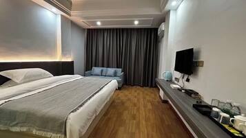 A hotel room with a large bed, a smaller sofa, a TV, and a bedside table with a tray of items.