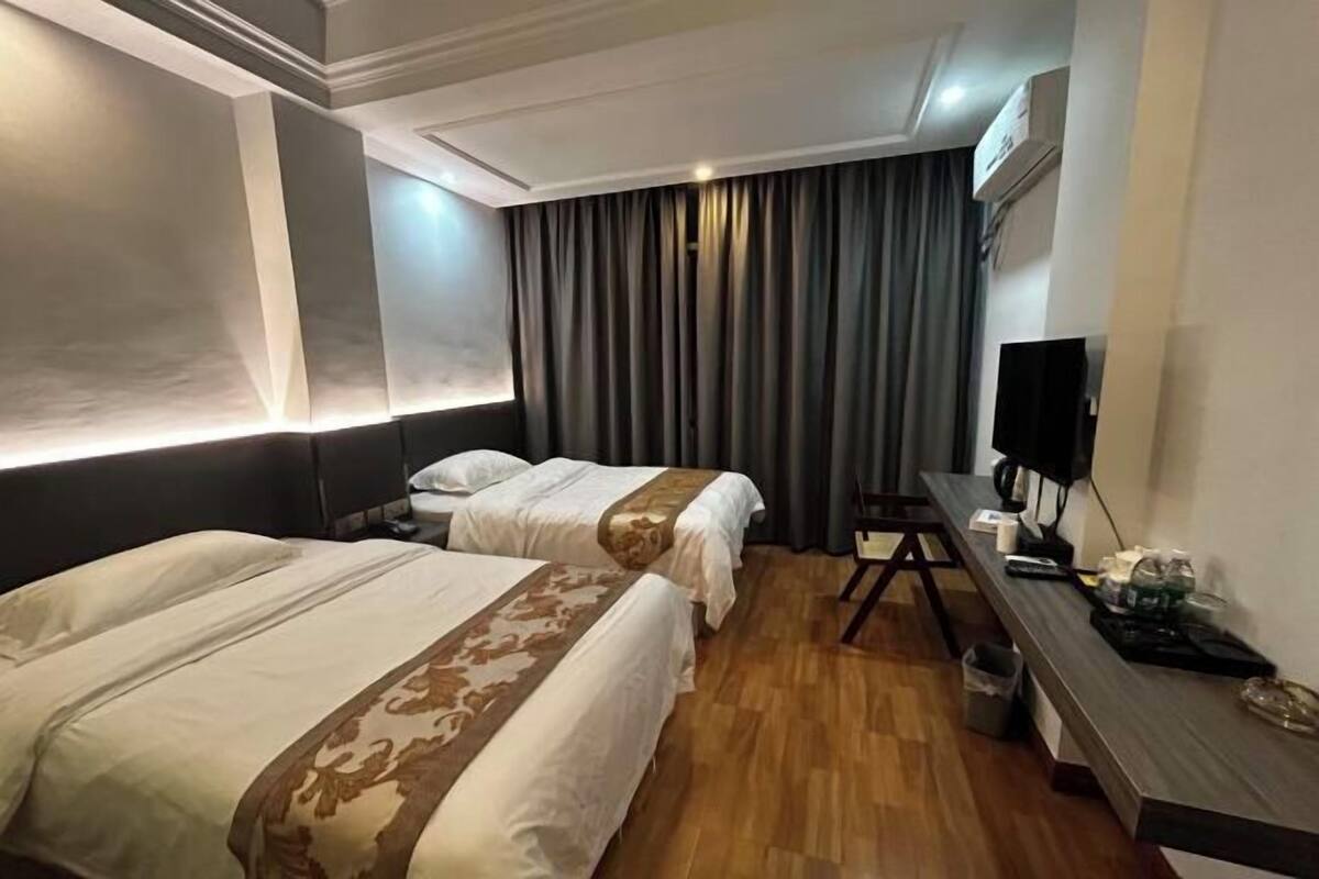 A hotel room with two beds, a desk, a TV, and a window with curtains.