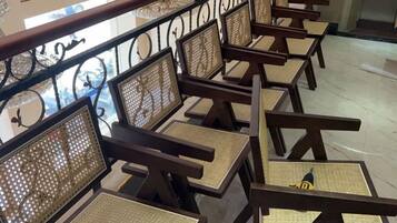 A row of wooden chairs with woven seats and backs, arranged in a row along a balcony railing.