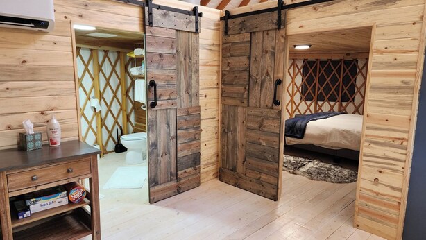 Una habitación rústica de madera con cama, un escritorio con silla y un baño con inodoro y lavabo.