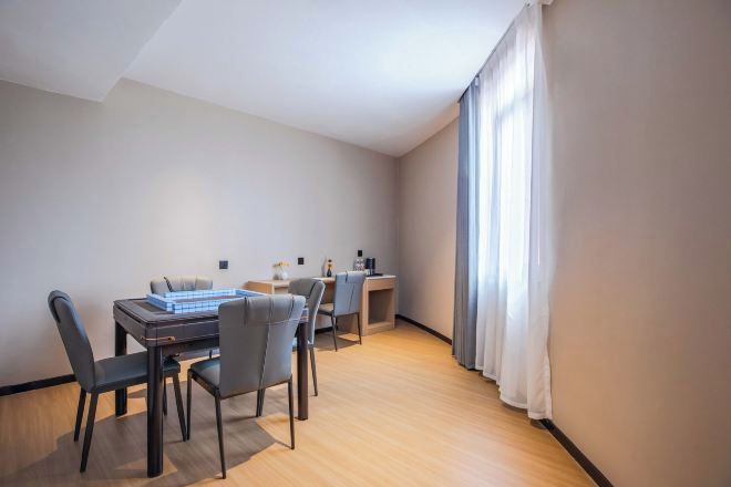 A modern, well-lit room with a dining table and chairs, a small desk, and a large window with curtains.
