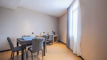 A modern, well-lit room with a dining table and chairs, a small desk, and a large window with curtains.