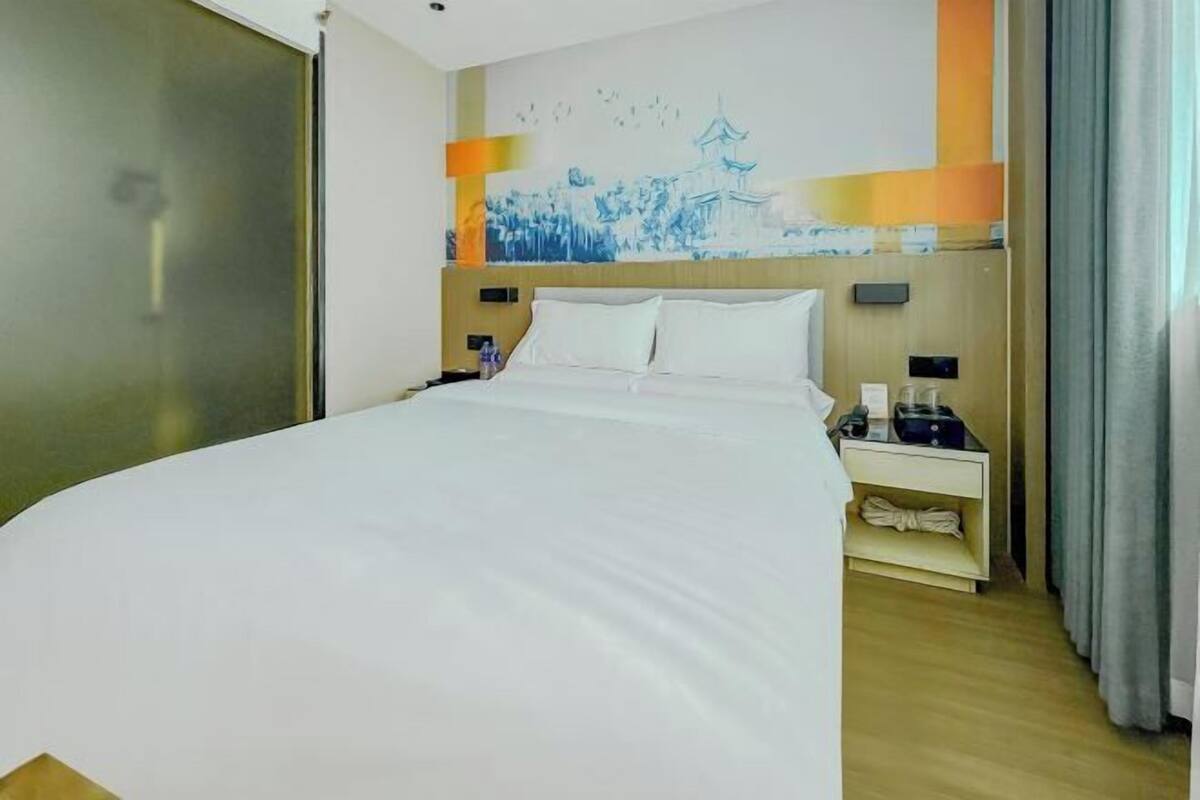 A hotel room with a large bed, a nightstand with a lamp, a wall-mounted TV, and a painting.
