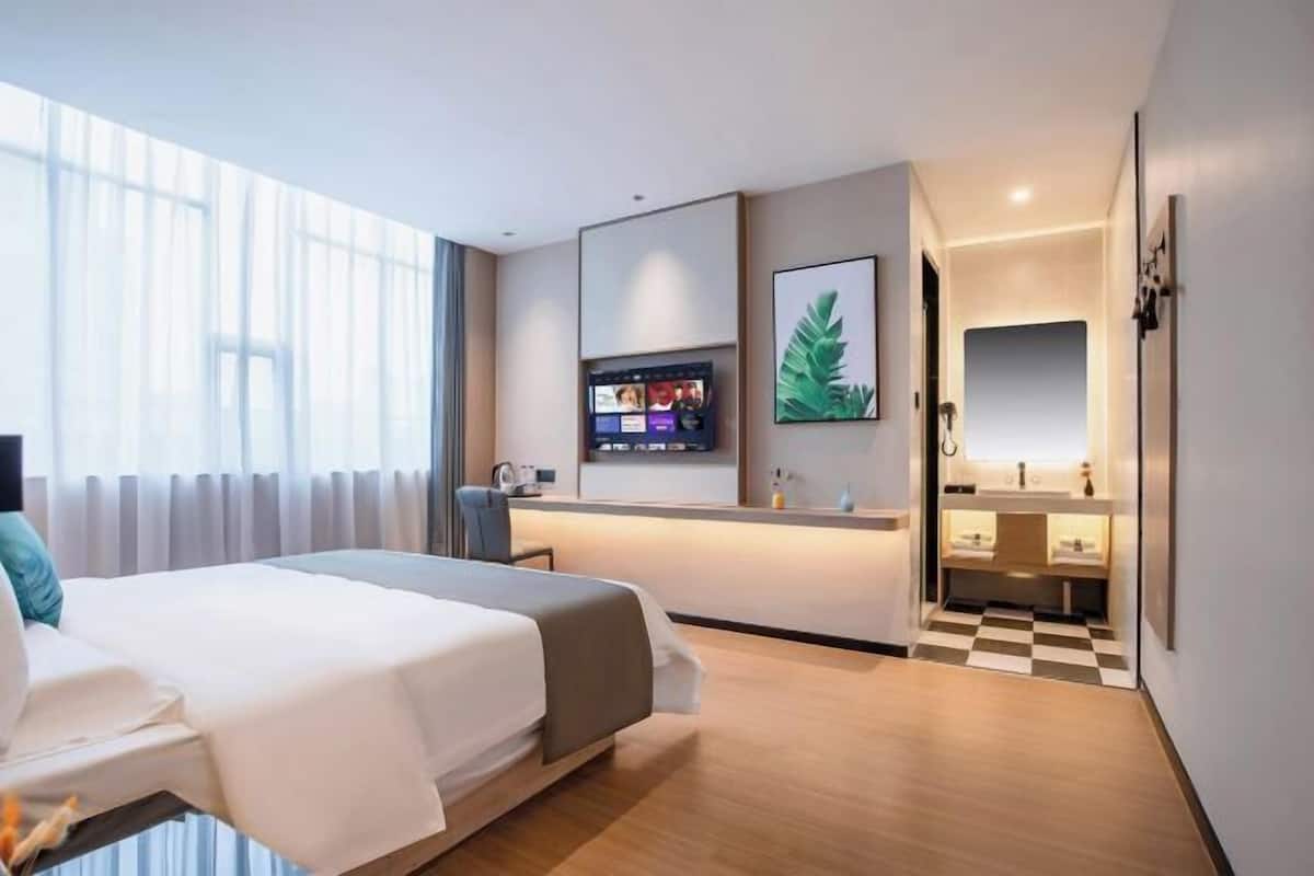 A modern hotel room with a bed, a desk, a TV, and a bathroom.