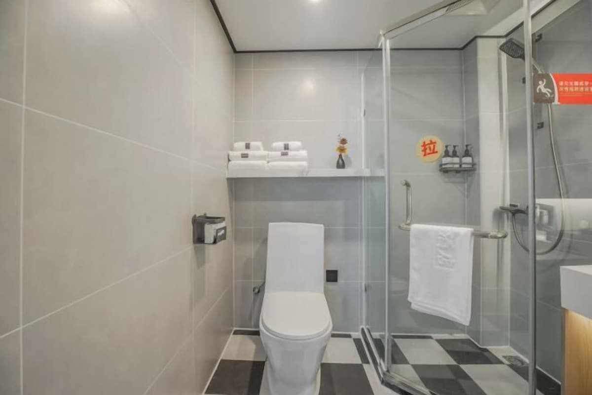 A modern bathroom with a toilet, a glass shower enclosure, and a shelf with toiletries.