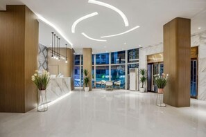 Een moderne hotellobby met een receptiebalie, een zithoek en grote ramen.