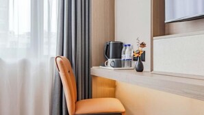 Une chambre d’hôtel avec un fauteuil moderne, une machine à café et une petite table sur laquelle se trouvent un vase et des bouteilles d’eau.