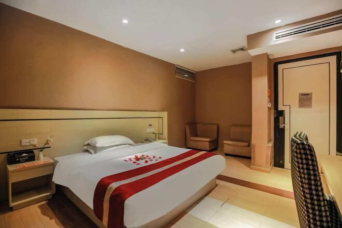 A hotel room with a large bed, a bedside table, a chair, and a wardrobe.