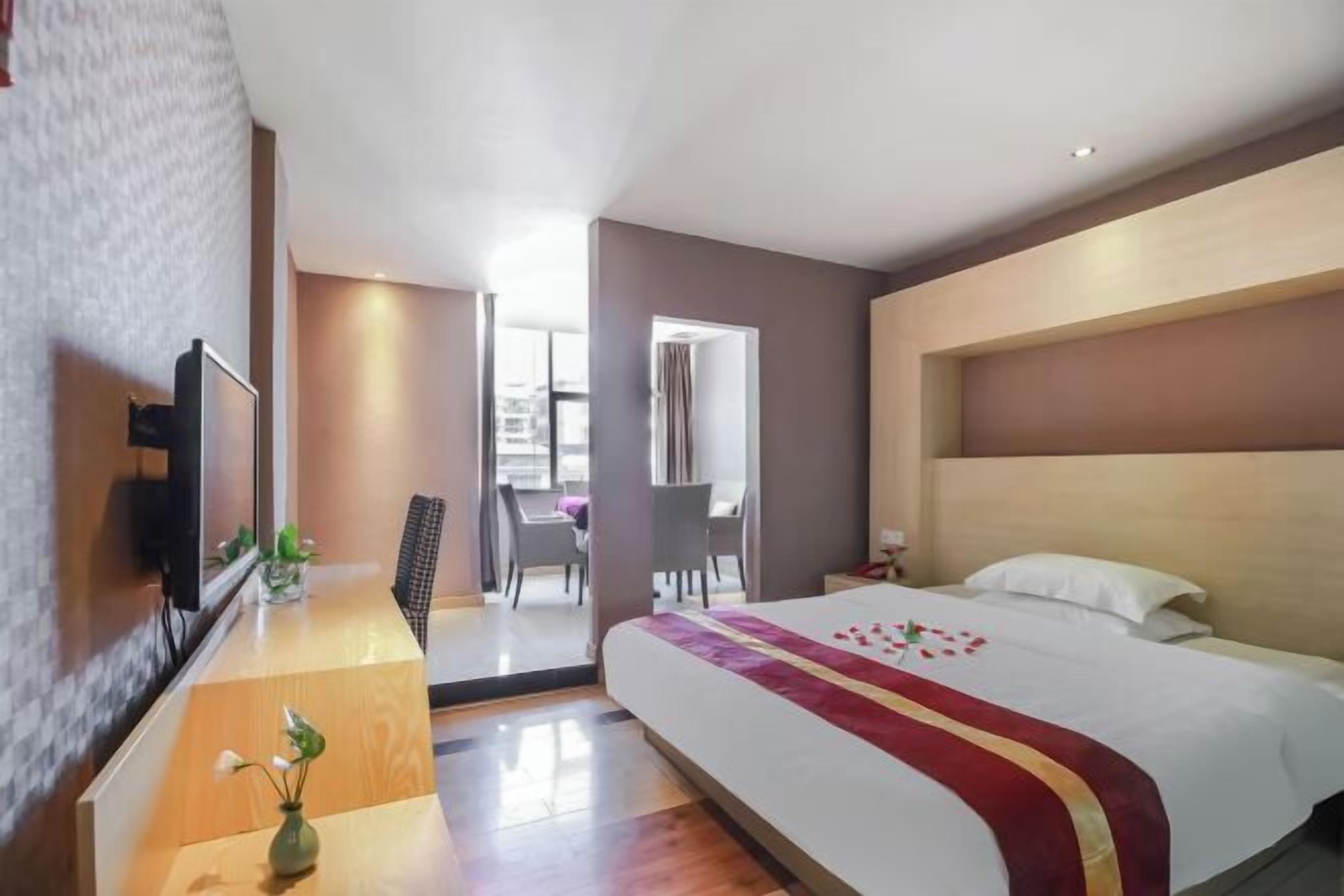 Ett hotellrum med en stor säng, en tv, ett skrivbord med en vas och utsikt över omgivningarna.