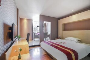 Habitación de hotel con una cama grande, televisión, escritorio con un florero y vistas al exterior.