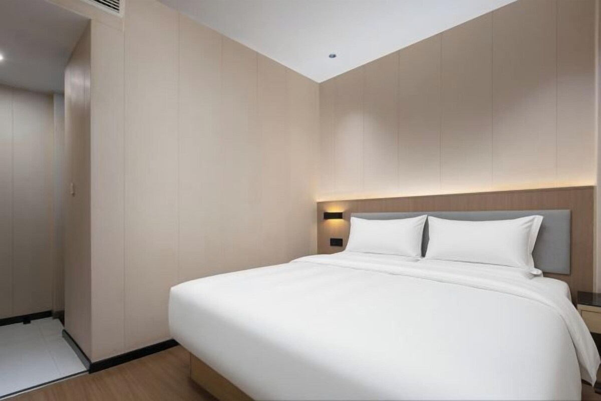 A hotel room with a large bed, a nightstand, and a wall-mounted light.