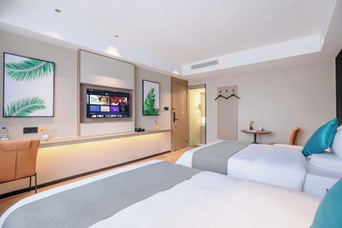 Una habitación de hotel con dos camas, un televisor, una mesita y un perchero.