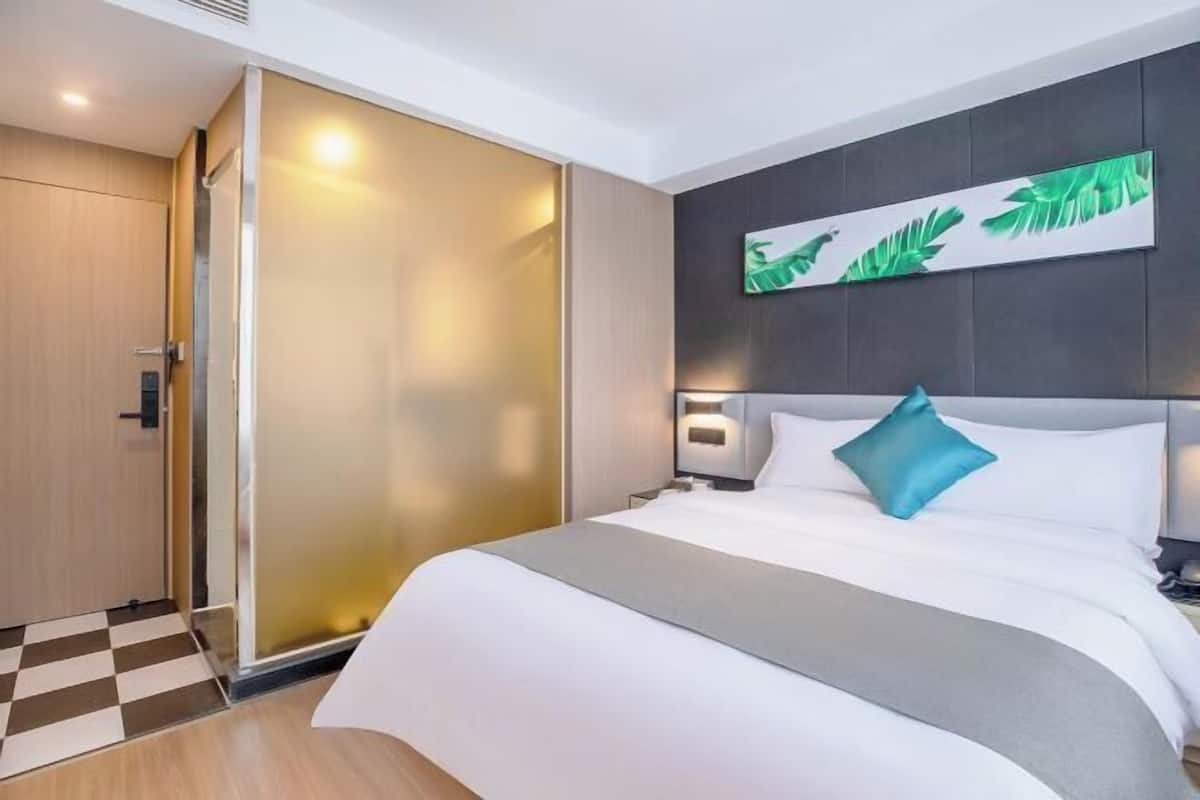 A hotel room with a bed, a wall-mounted artwork, a nightstand, and a sliding door.