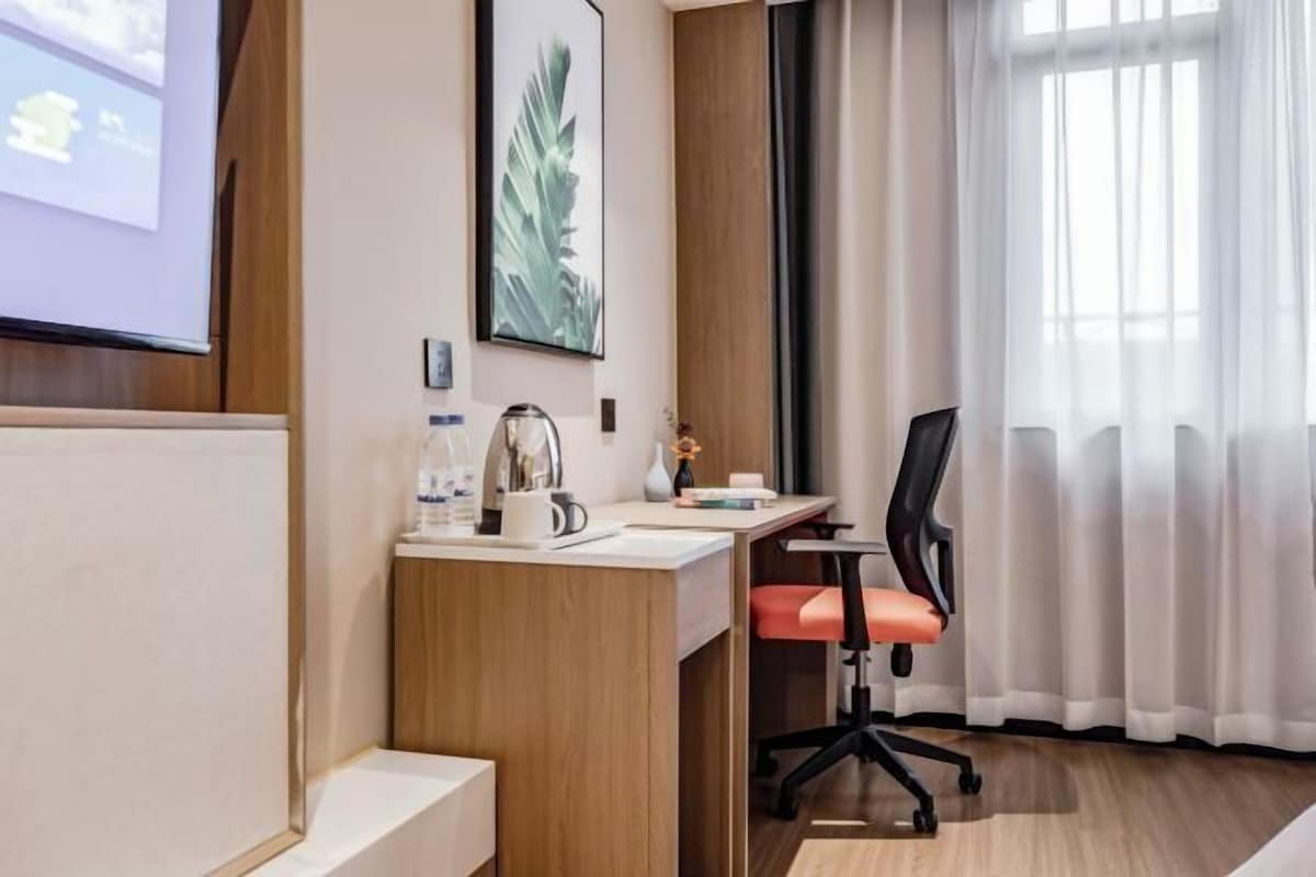 Hotelkamer met een houten bureau, een rode stoel, een scherm voor een projector en een groot raam met gordijnen.