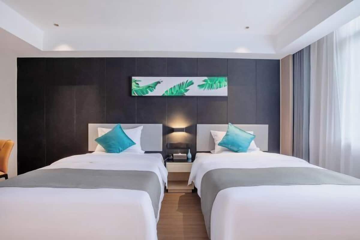 A hotel room with two beds, a nightstand, a wall-mounted artwork, and a window with curtains.