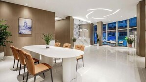 Un hall d’hôtel moderne avec une grande table ovale, des sièges confortables et une vue sur la ville grâce à de grandes fenêtres.