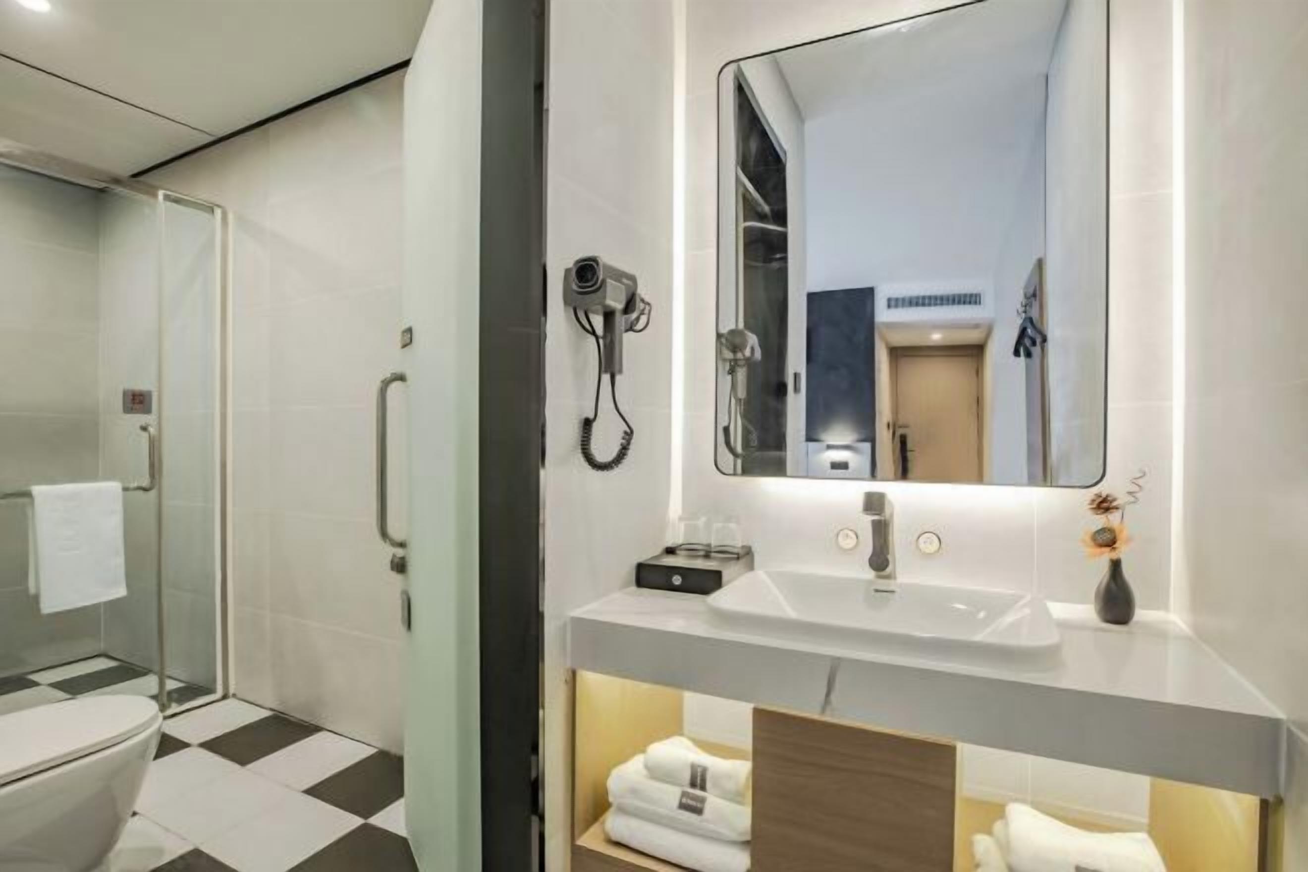 A modern bathroom with a glass shower enclosure, a white sink with a mirror above it, and neatly folded towels on a shelf.