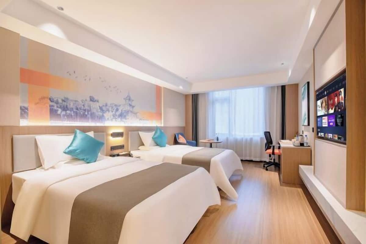 A hotel room with two beds, a desk, a chair, and a large window.