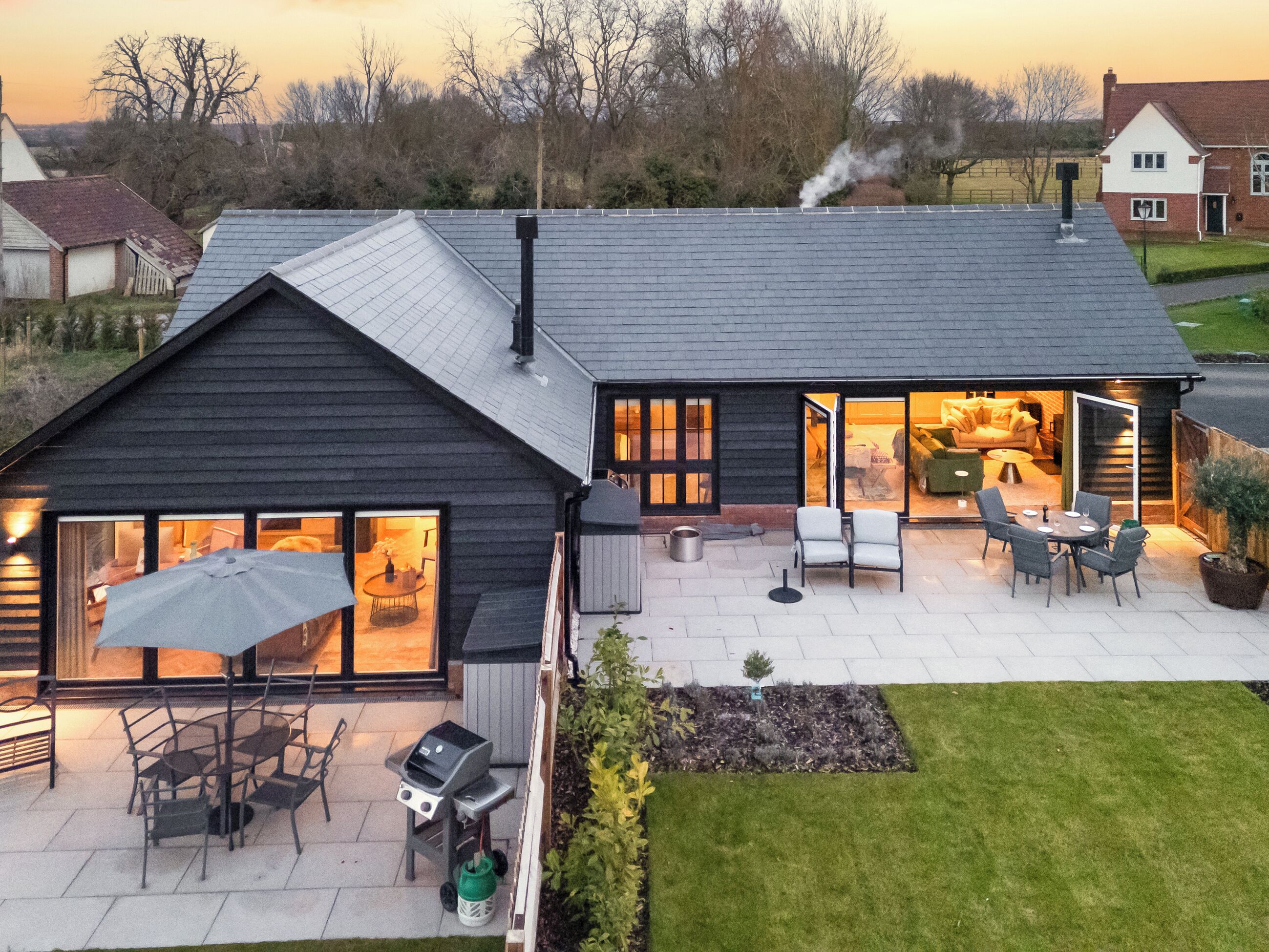 Een modern huis met een terras, zitplaatsen buiten en een barbecuehoek.