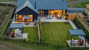 A modern house with a large patio, a lawn, and a covered outdoor seating area.